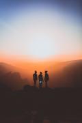 Three people standing together at sunrise overlooking a mountain landscape, symbolizing support, hope, and recovery