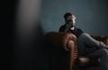 Man sitting alone on a couch with his hand covering his face, reflecting emotional distress and mental health challenges