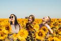 Three women smiling and enjoying time together in a vibrant sunflower field