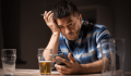 Man sitting alone with a drink, appearing stressed and emotionally overwhelmed