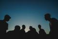 Silhouettes of people gathered outdoors at sunset, representing peer support, community connection, group therapy, and recovery fellowship
