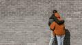 Two people embracing in a supportive hug against a brick wall, representing connection and emotional support