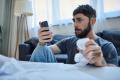 Stressed man looking at smartphone while holding bills after mobile gambling losses