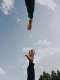 Two hands reaching toward each other against a bright sky with scattered clouds