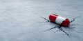 Cracked red and white capsule on fractured concrete representing mitragynine pseudoindoxyl (pseudo) drug risks and addiction dangers.