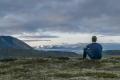 Person sitting on a hillside overlooking mountains and a valley during a quiet moment of reflection