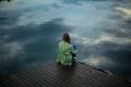Person sitting alone on a wooden dock overlooking calm water in a moment of reflection
