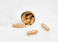 Open supplement bottle with capsules scattered on a white surface, representing nutritional support and wellness