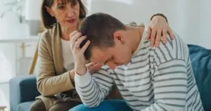 Older woman comforting a distressed young man during a serious family conversation about addiction and emotional healing