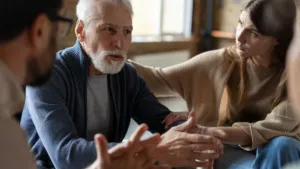 Older man speaking in a support group while a younger woman sits beside him, showing connection and support in addiction recovery
