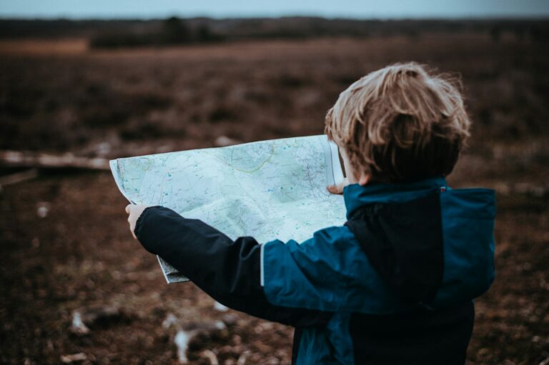 Person holding a map outdoors while exploring a natural landscape, symbolizing personal growth, direction, and recovery journeys
