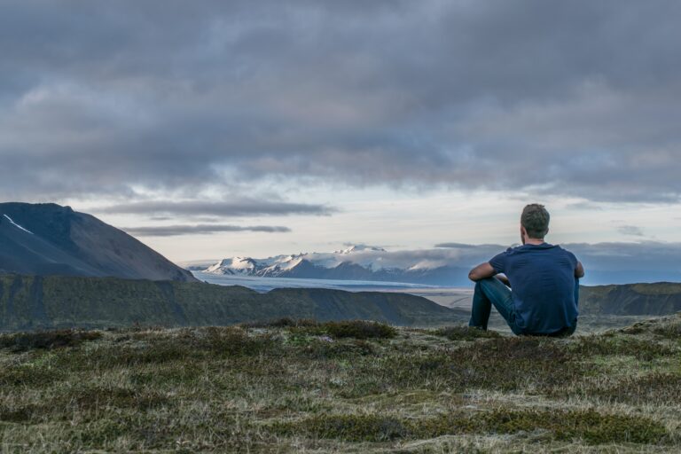 Person sitting on a hillside overlooking mountains and a valley during a quiet moment of reflection