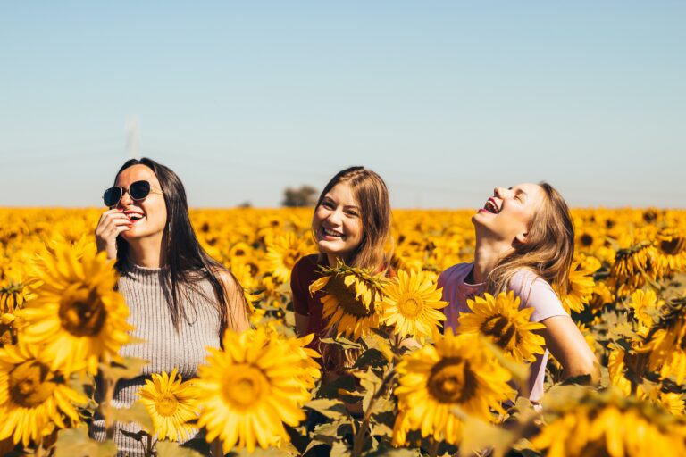 Three women smiling and enjoying time together in a vibrant sunflower field