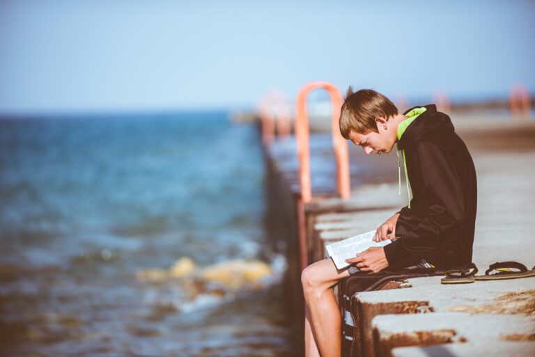 Young person reading a book by the water, representing self-reflection, personal growth, and recovery education