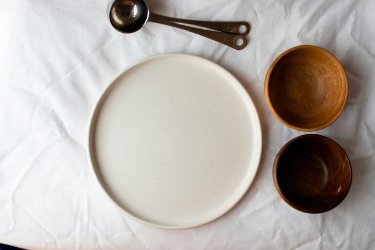 Minimal place setting with an empty plate, bowls, and measuring spoons arranged on a white tablecloth