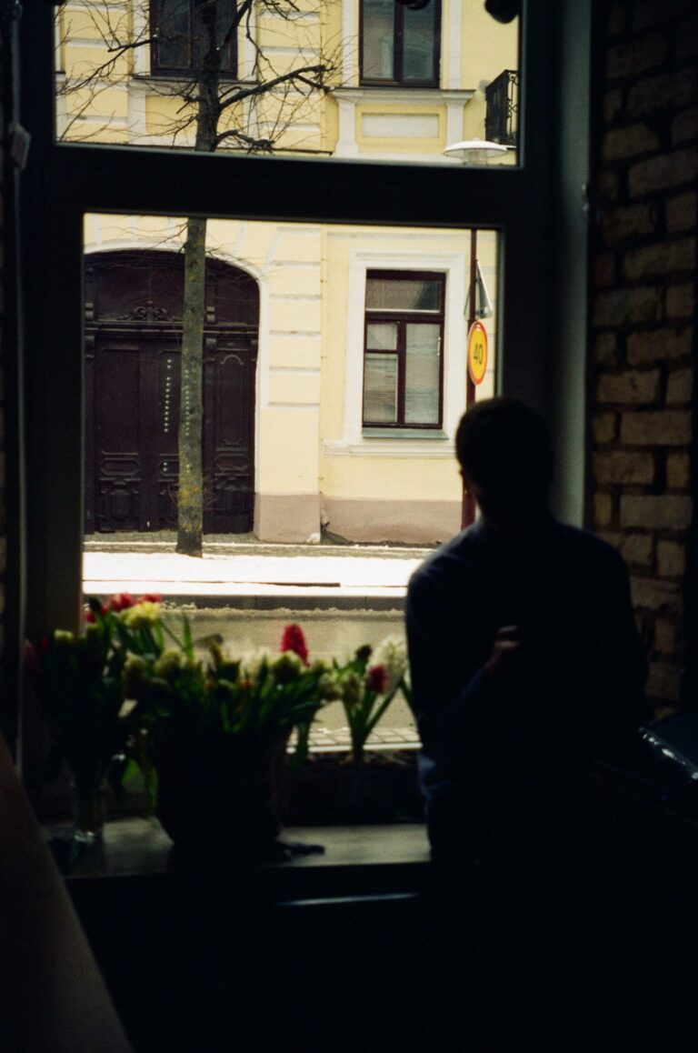 Person standing by a window looking outside, representing loneliness, reflection, and emotional healing