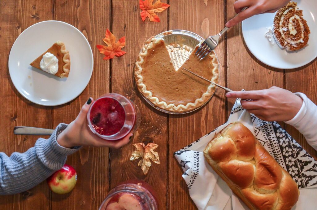 People sharing pie, bread, and drinks around a table during a communal meal
