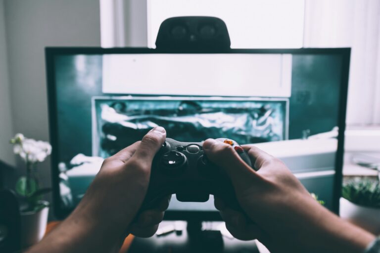 Person holding a video game controller while playing on a computer monitor, representing gaming habits, screen time, and digital entertainment