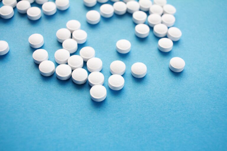White prescription tablets scattered across a blue surface, representing medication use and substance dependence
