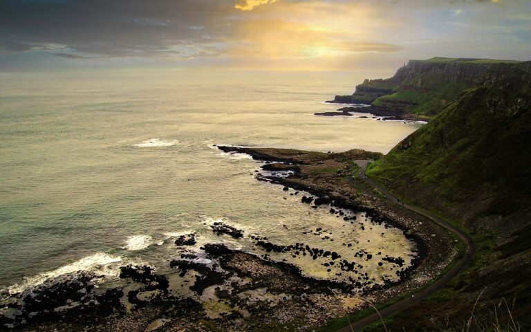 Scenic ocean coastline with green cliffs, rocky shore, and sunset sky