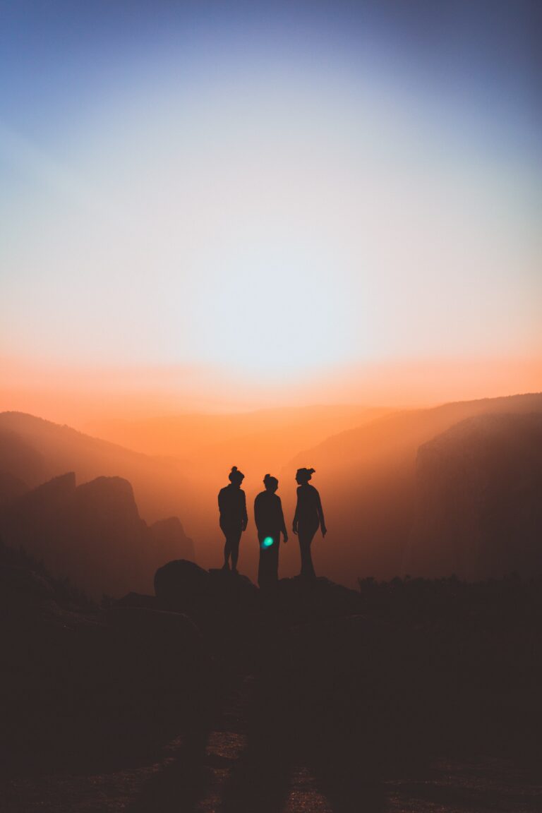 Three people standing together at sunrise overlooking a mountain landscape, symbolizing support, hope, and recovery
