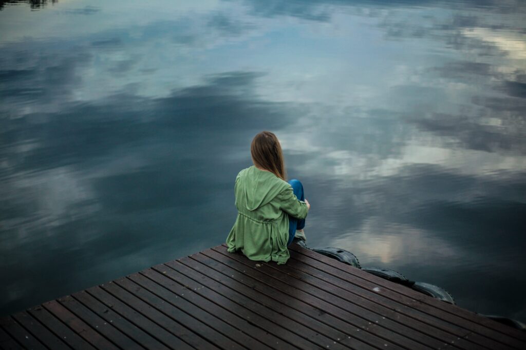 Person sitting alone on a wooden dock overlooking calm water in a moment of reflection