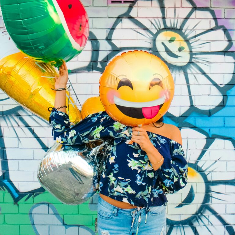 Person holding colorful balloons and a smiling emoji balloon, representing happiness, positive emotions, and recovery progress