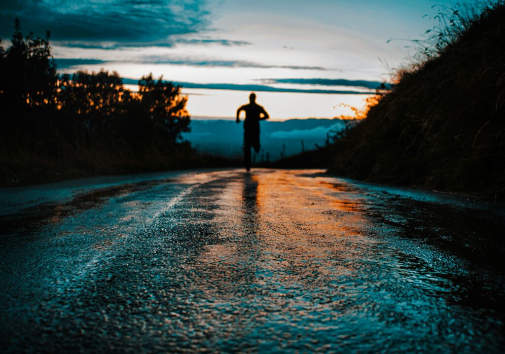 Person running on a wet road at sunrise, symbolizing perseverance, healthy habits, recovery, and personal growth