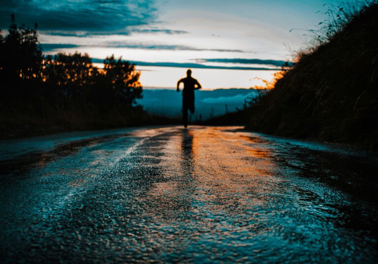 Person running on a wet road at sunrise, symbolizing perseverance, healthy habits, recovery, and personal growth