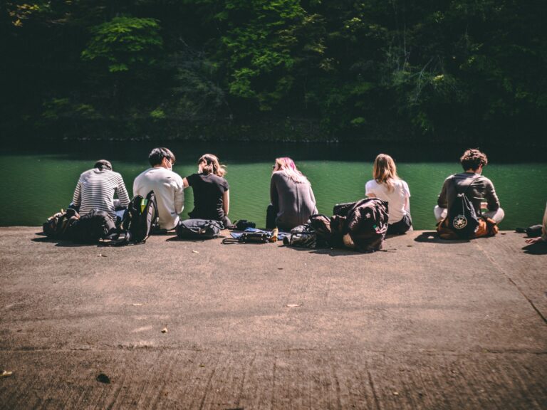 Group of people sitting together beside a lake surrounded by trees and nature