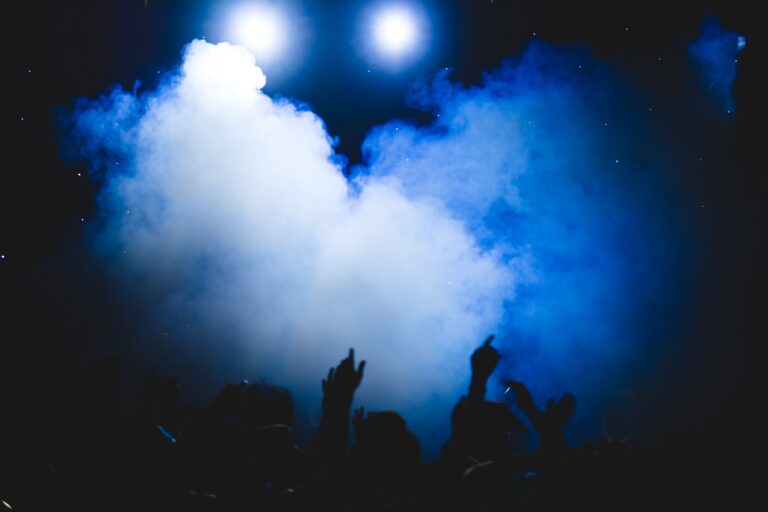 Crowd gathered beneath bright stage lights and smoke effects at a live concert or nightlife event