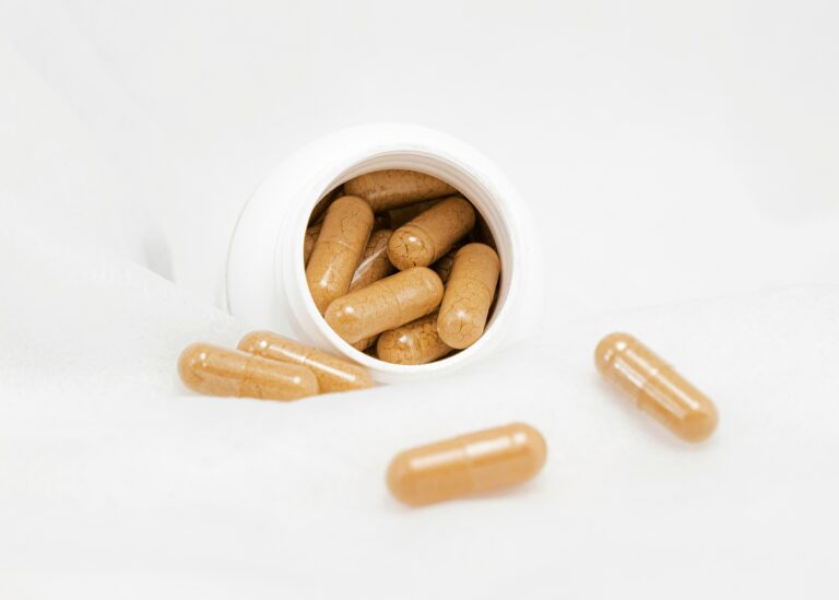 Open supplement bottle with capsules scattered on a white surface, representing nutritional support and wellness