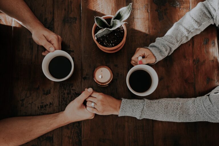 People holding hands over coffee during a supportive conversation about recovery, mental health, and emotional healing