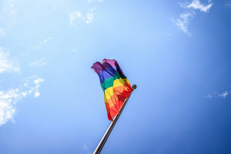 Rainbow pride flag flying against a blue sky, representing inclusion, acceptance, and community support
