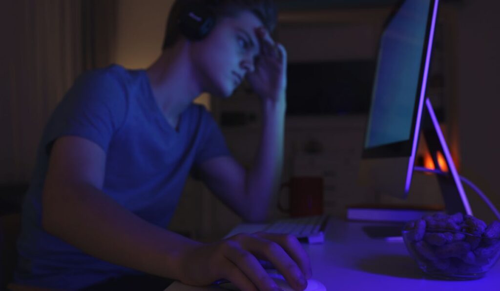 Young person using a computer late at night, showing excessive screen time and digital dependence
