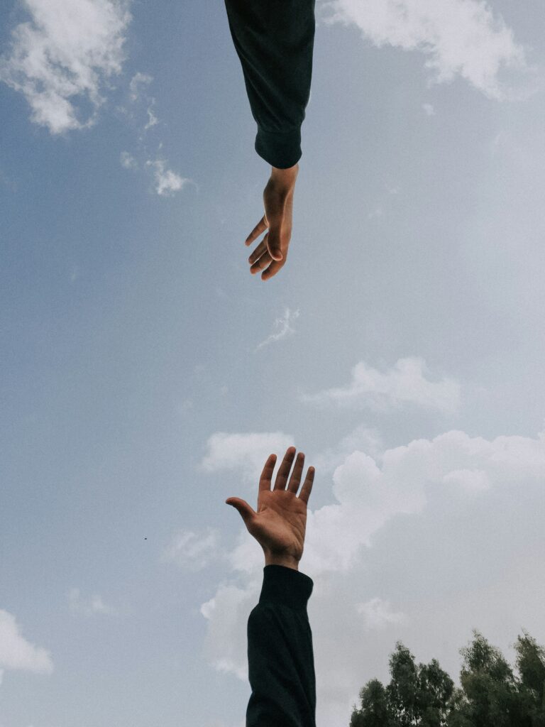 Two hands reaching toward each other against a bright sky with scattered clouds