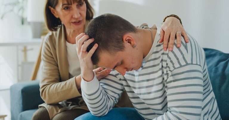 Older woman comforting a distressed young man during a serious family conversation about addiction and emotional healing